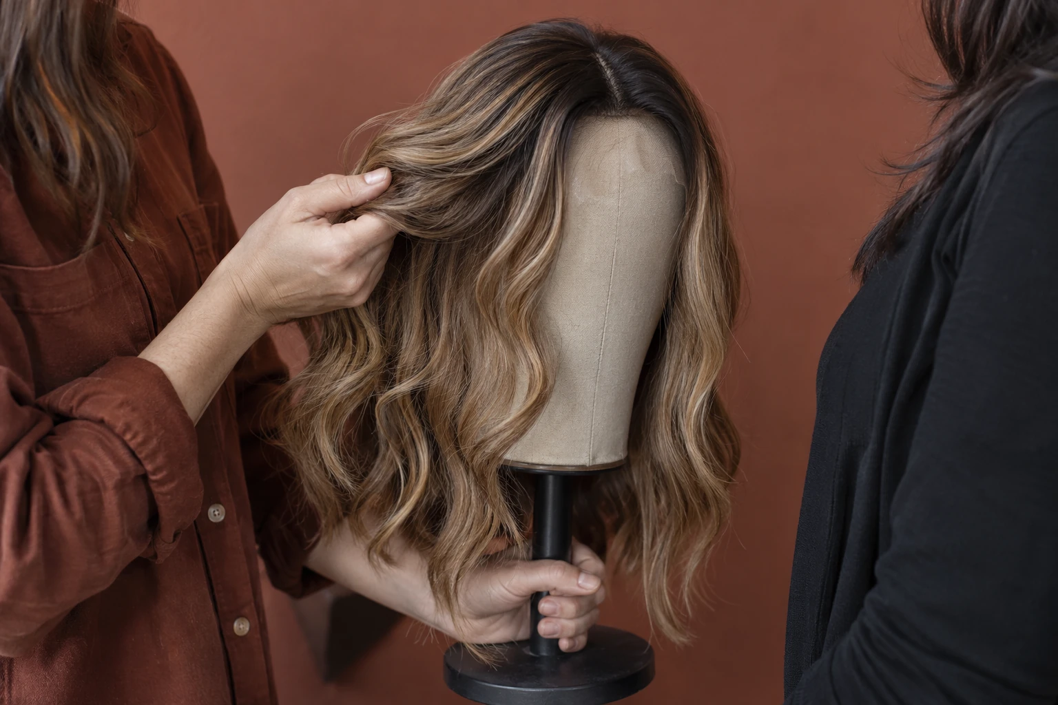 A wig display demonstration showing a section of dark-rooted balayage hair